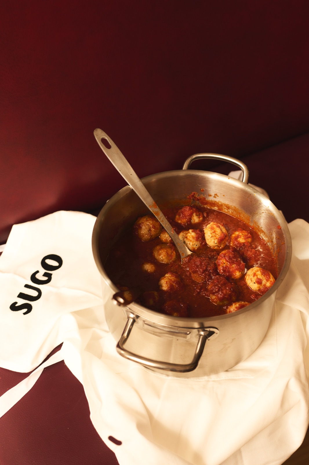 Faitout de polpette en sauce tomate posé sur un tablier SUGO